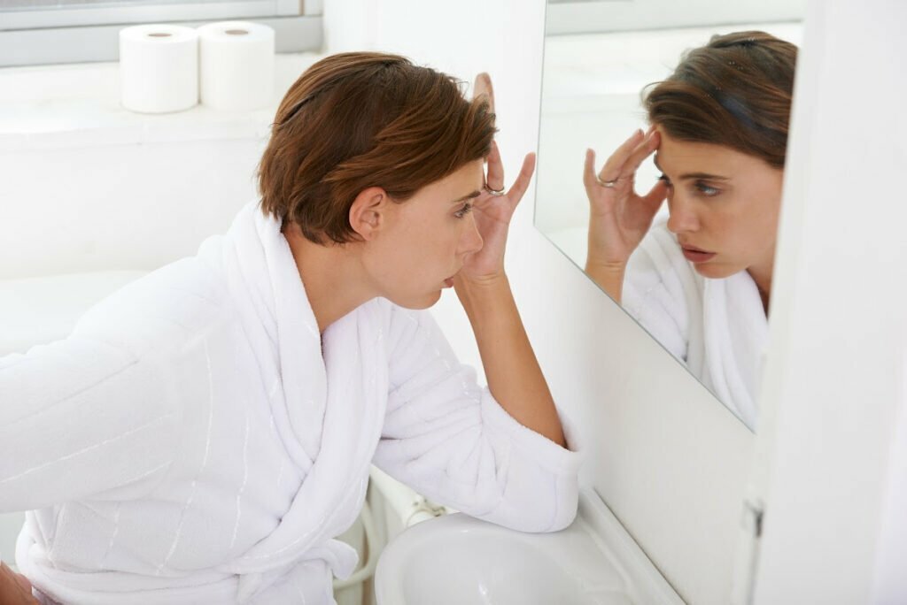 Tired Woman Looking in Mirror Wanting to Refresh Appearance Post-Pandemic with Non-Surgical Facial Procedures