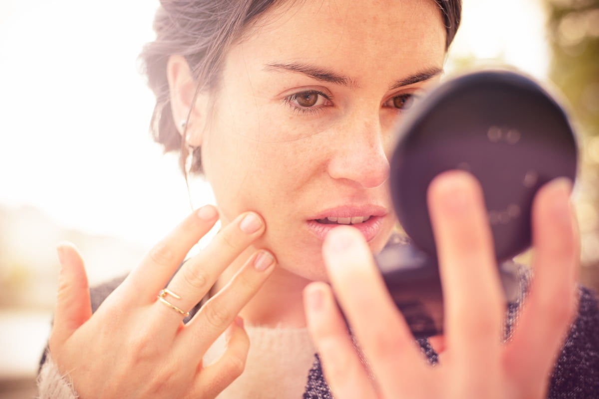 Woman looking at sun damage on skin in mirror